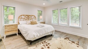 A bedroom with a bed, nightstands, a ceiling fan, and large windows with blinds. - Golf, Dine & Swim: Sleek Palmetto Dunes Home! (Hilton Head Island)