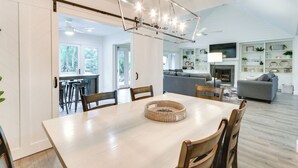 A dining area with a wooden table and chairs, a woven centerpiece, and a modern chandelier. - Golf, Dine & Swim: Sleek Palmetto Dunes Home! (Hilton Head Island)