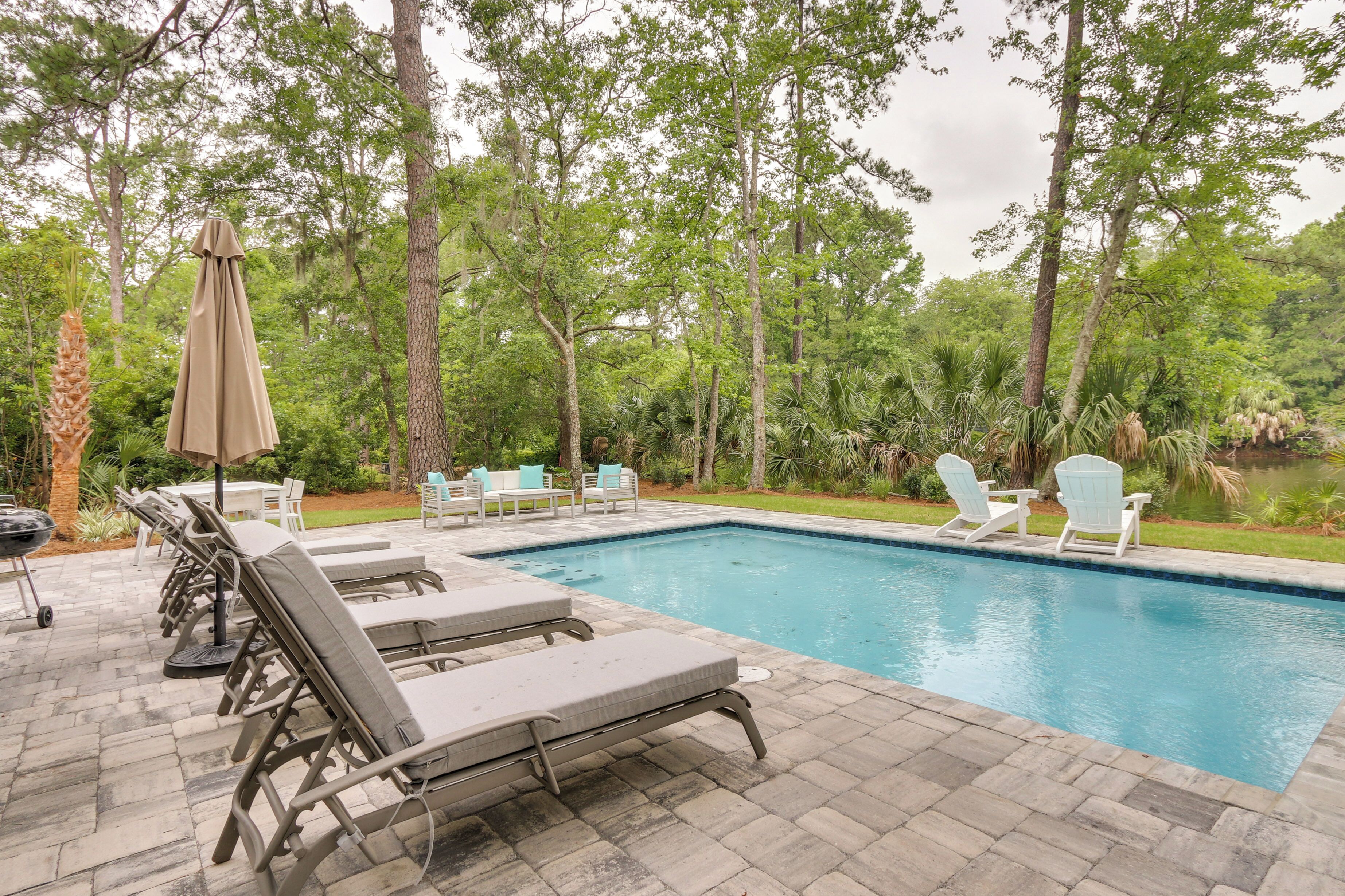 A swimming pool with lounge chairs and a table, surrounded by trees.