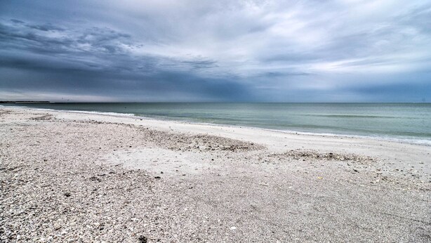 Ein Strand mit Kieselsteinen und einem ruhigen Meer unter einem bewölkten Himmel.