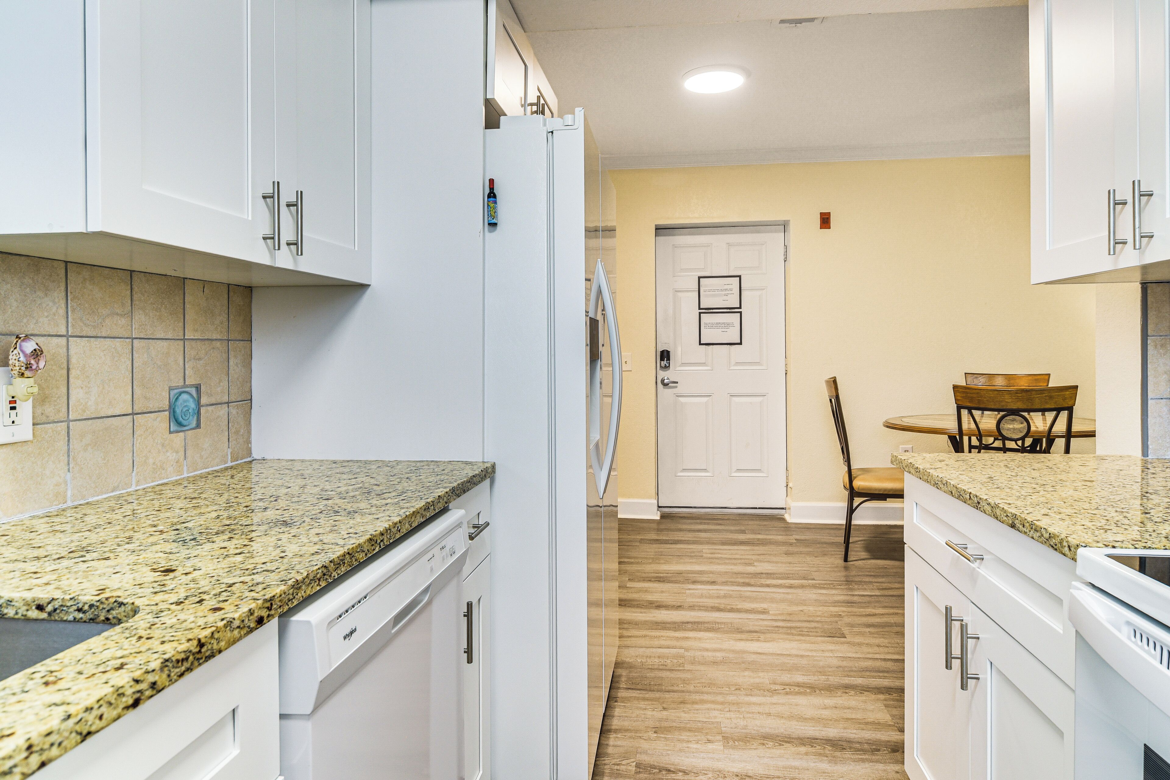 A kitchen with white cabinets, granite countertops, a dishwasher, and a wooden floor.