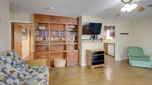 Una sala de estar con una estantería de madera, un televisor, un sillón verde y un mueble bajo.