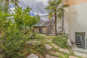 A courtyard with stone steps leading to a building entrance, surrounded by greenery and a palm tree. - Casa Stella in Varenna (Varenna)