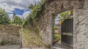 Ein Steinhaus mit einem Metallgitter, einem Pflasterweg und einer Steinmauer.