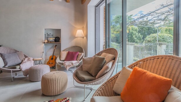 Ein modernes Wohnzimmer mit Rattanmöbeln, einer Gitarre und Blick ins Grüne.