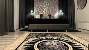 A bedroom with a large bed, dark curtains, a patterned wall, and a round rug with a sun design. - 1 Bed Flat - Sleeps 2 - Jacuzzi - Parking - Wifi (Birmingham)