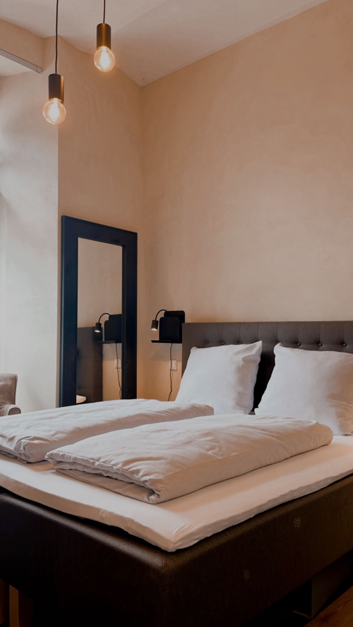 Un dormitorio moderno con una cama grande, un cabecero oscuro y dos lámparas colgantes.