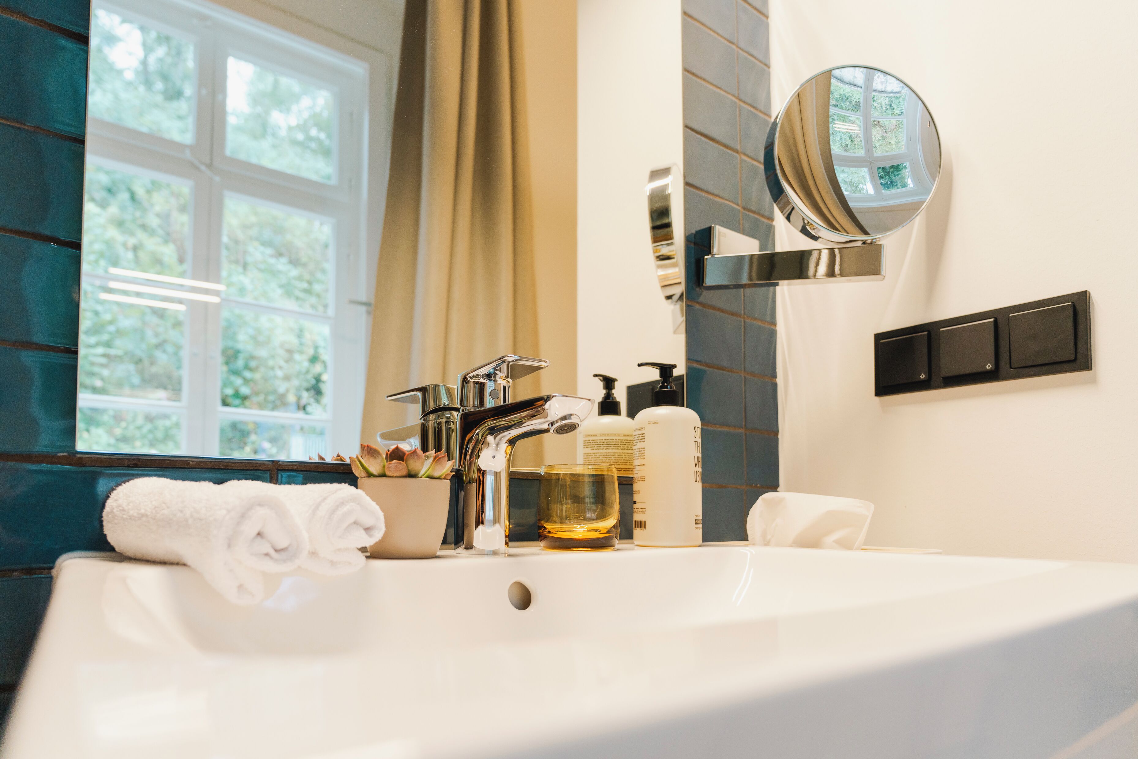 A modern bathroom with a large white sink, a mirror, and a window with curtains.