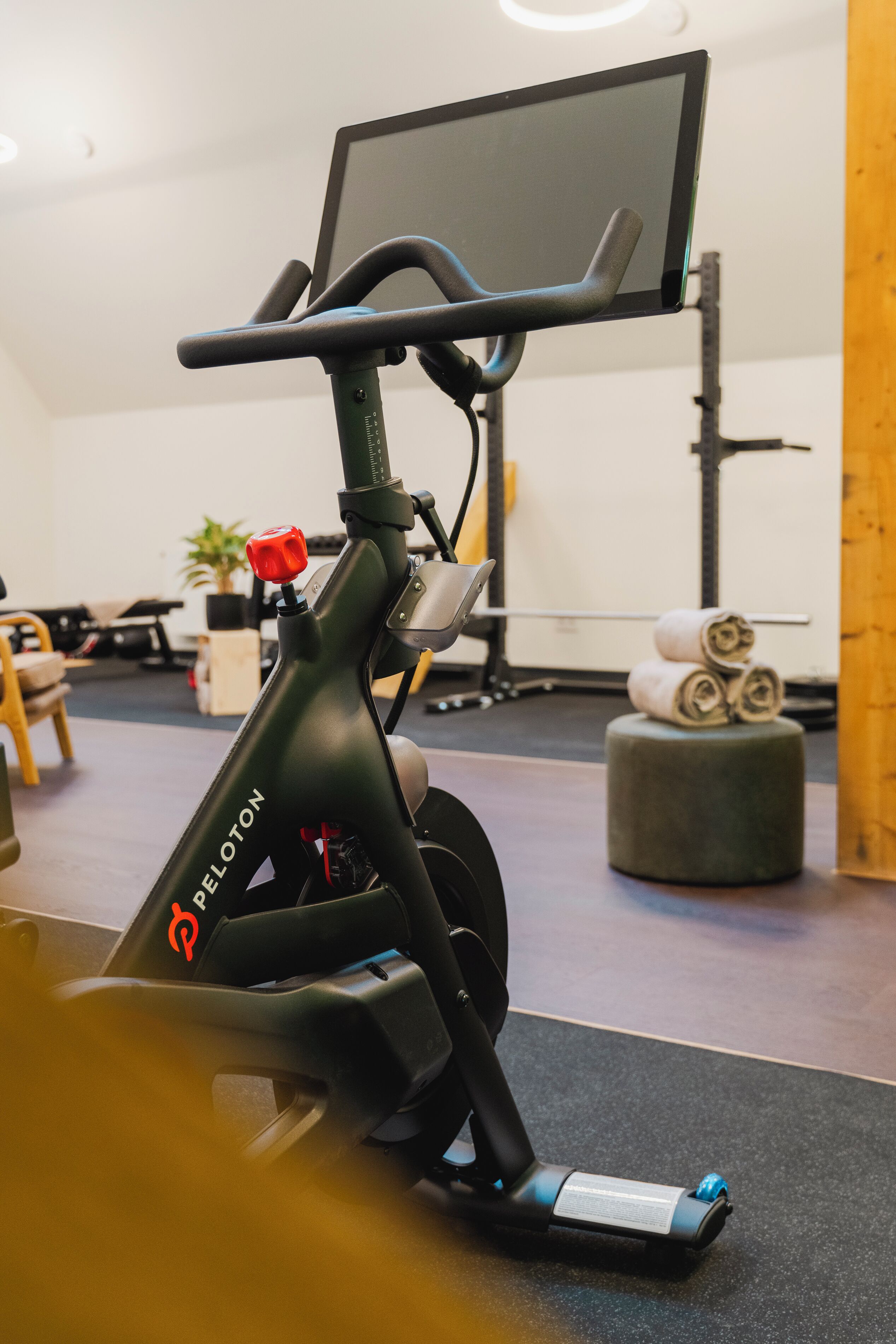 An exercise bike with a digital display and a red knob, placed in a room with a grey floor and a wooden column.