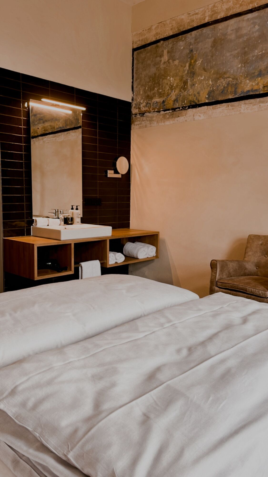 Habitación de hotel con una cama grande, una tocador de madera con espejo, un lavamanos y una silla.
