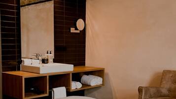 Habitación de hotel con una cama grande, una tocador de madera con espejo, un lavamanos y una silla.