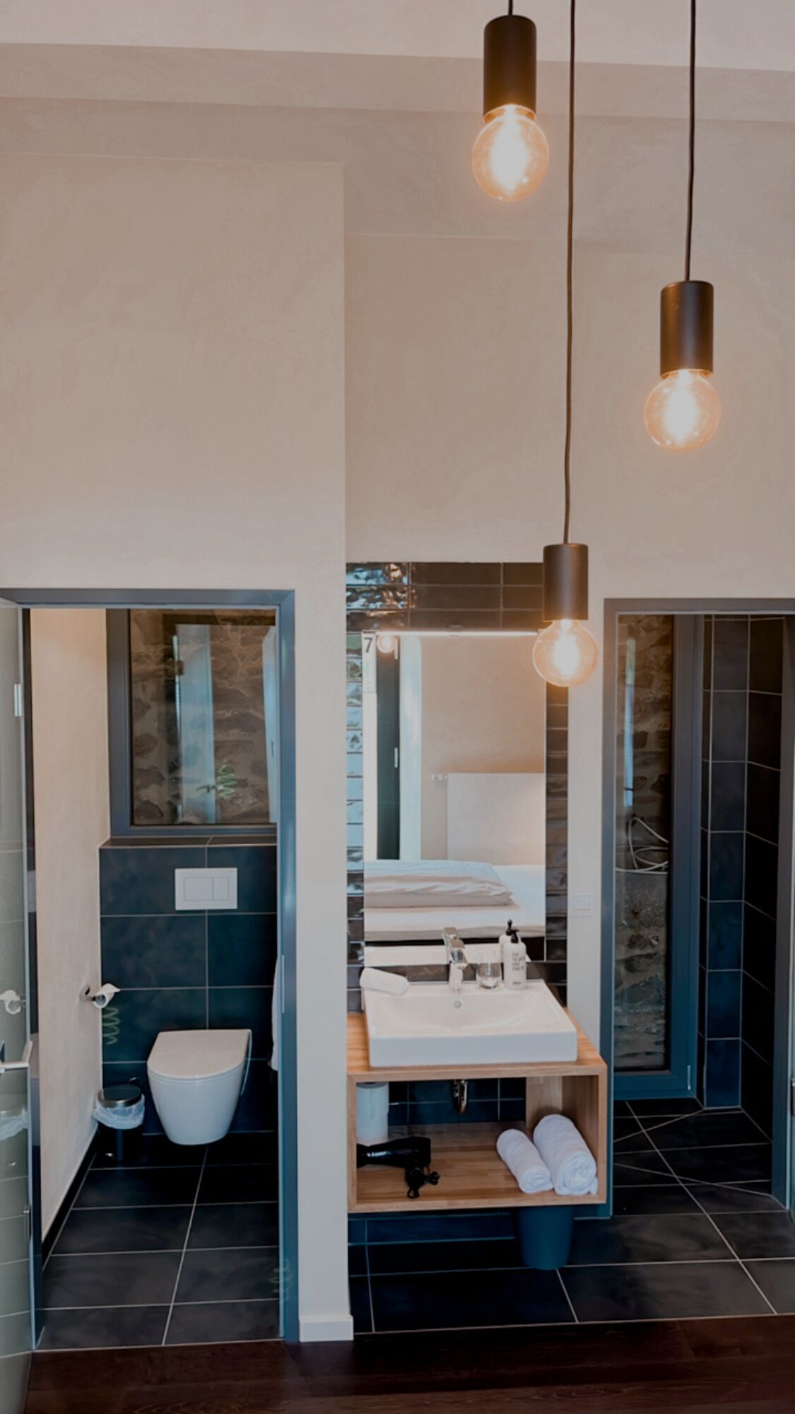 Een moderne badkamer met toilet, wastafel en douchegedeelte. Boven de wastafel hangen er hanglampen.
