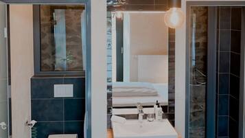 Een moderne badkamer met toilet, wastafel en douchegedeelte. Boven de wastafel hangen er hanglampen.
