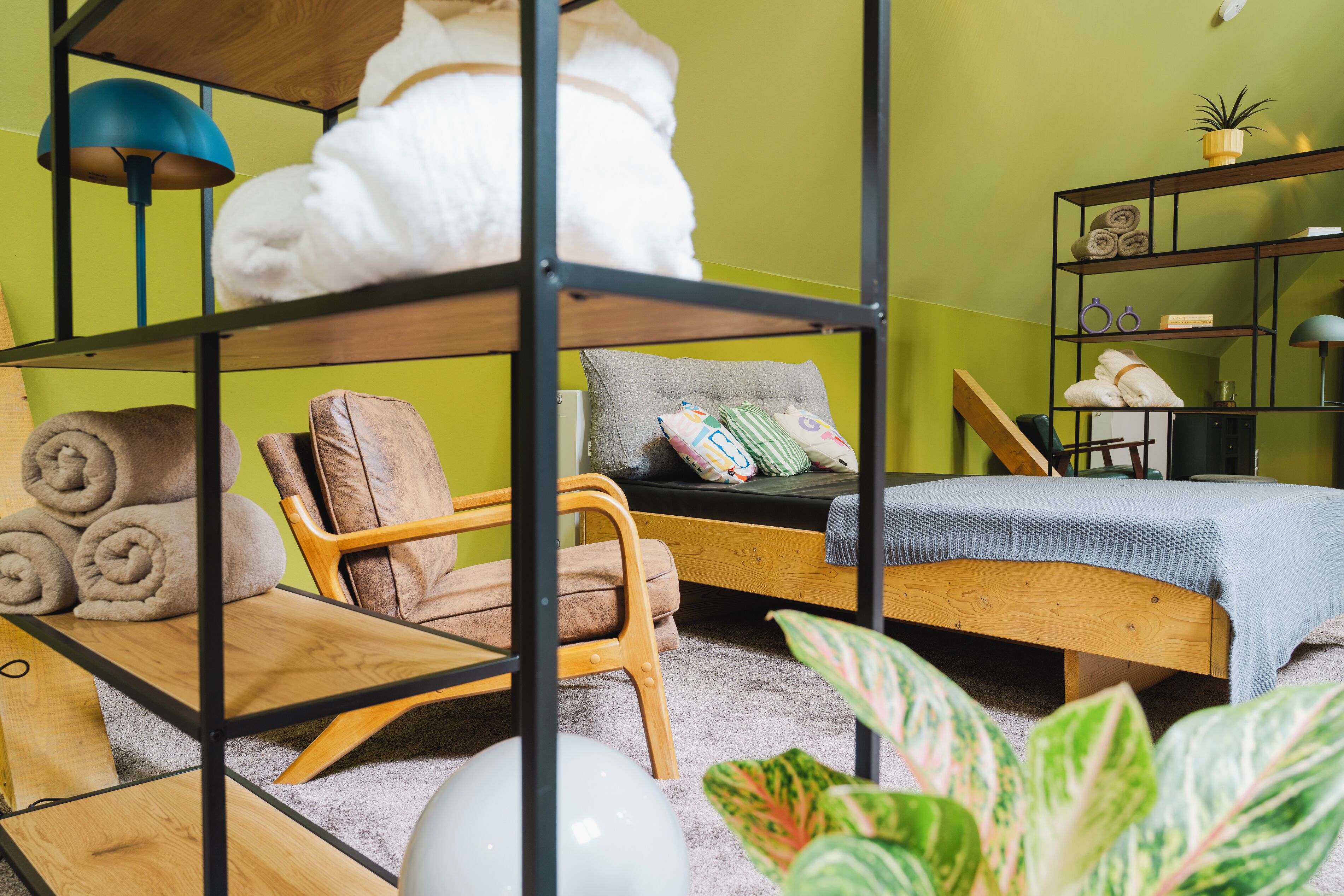 Una habitación acogedora con una litera, una silla, una mesita y un estante con toallas y una planta.