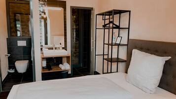 A hotel room with a bed, a bathroom with a sink, and a storage unit with shelves.
