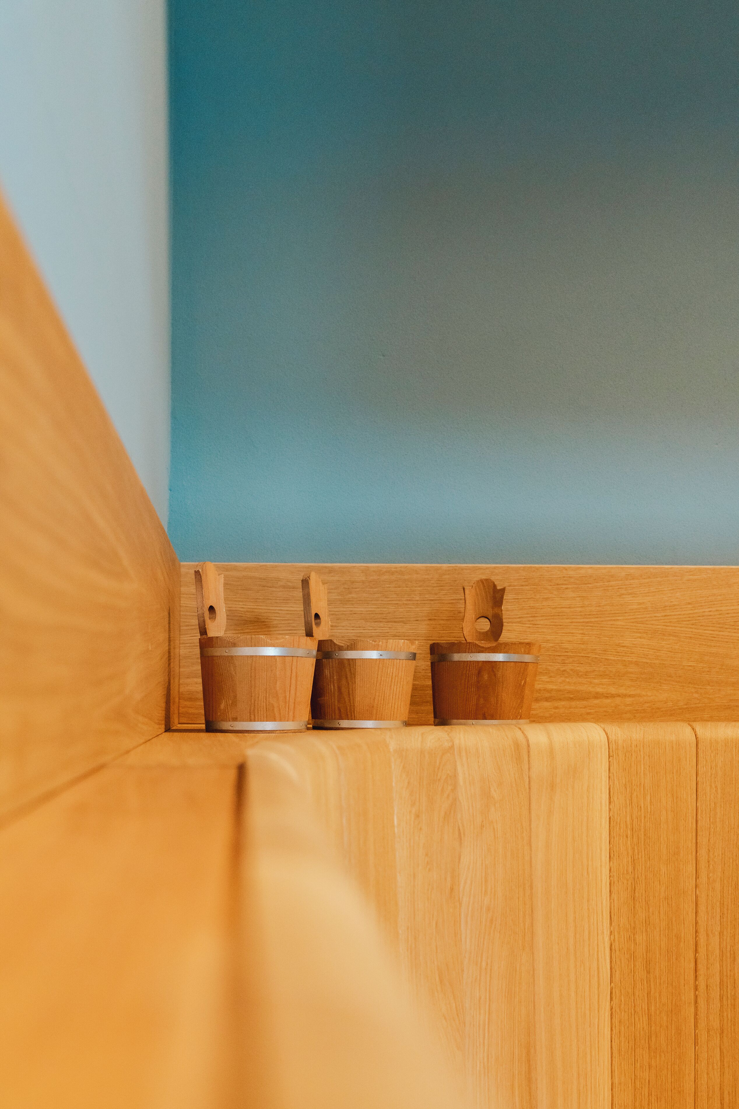 Rincón de una habitación con un banco de madera y tres cubos de madera, frente a una pared azul.