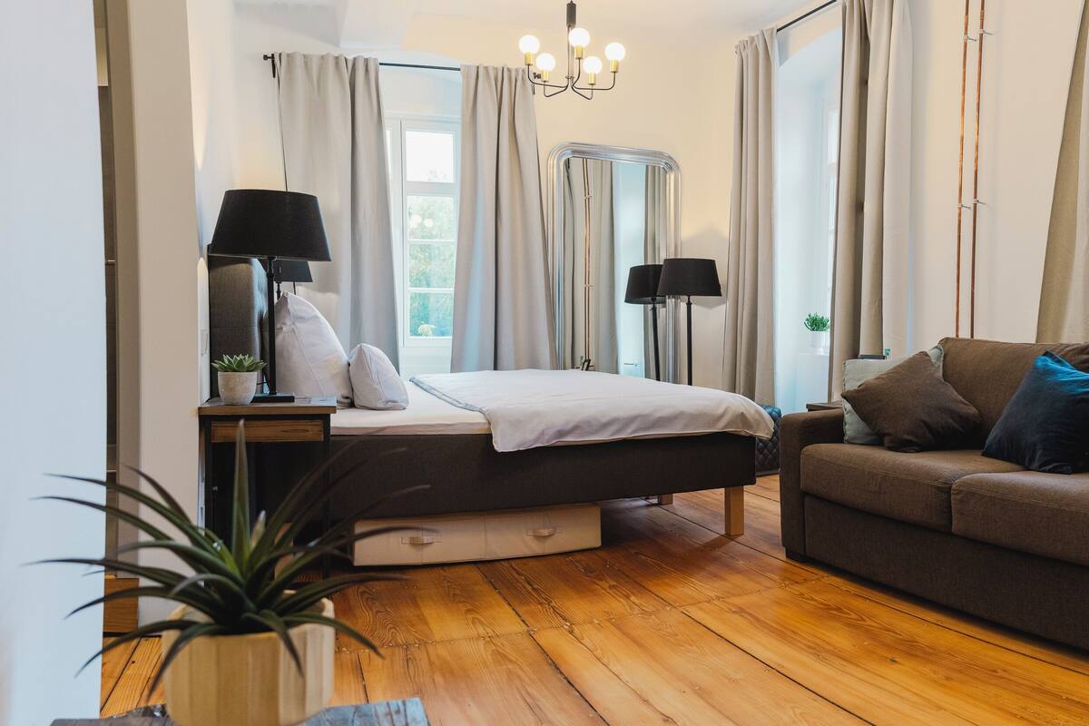 Une chambre à coucher avec un lit, un canapé, une table de chevet, une lampe et une fenêtre avec des rideaux.