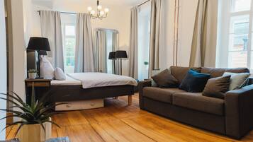 Quarto com cama, sofá, mesa de cabeceira, luminária e janela com cortinas.