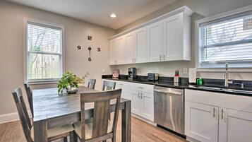 A modern kitchen with white cabinets, a wooden dining table, and a potted plant.