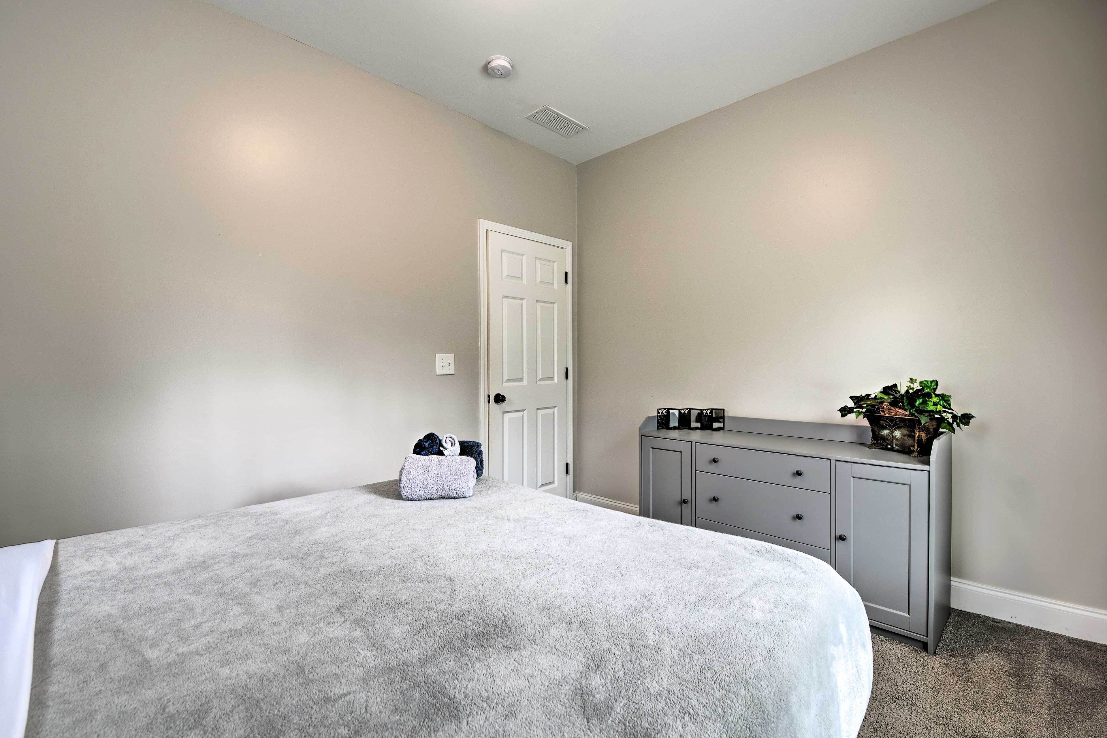 A bedroom with a large bed, a dresser, a door, and a plant on the dresser.