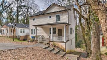 A two-story house with a front porch, a small front yard, and a driveway leading to the house.
