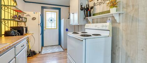 A kitchen with white cabinets, a stove, and a broom. There is a door with a window and a sign above it.