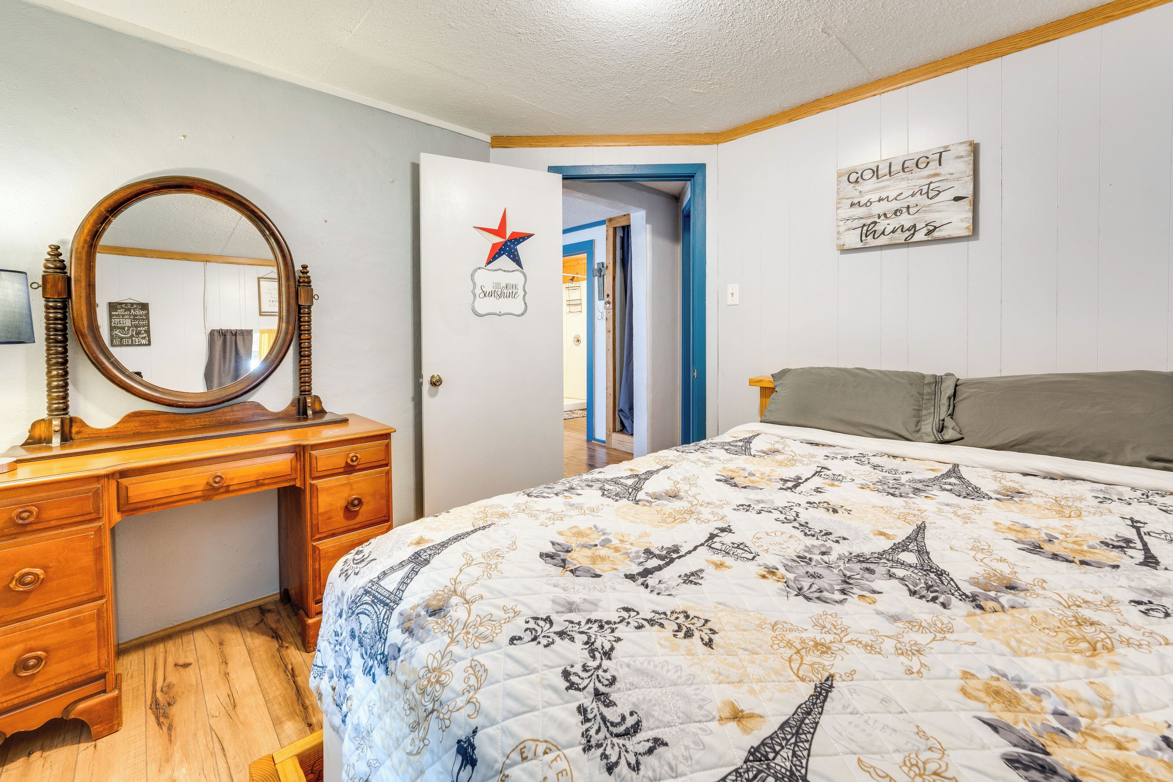 A bedroom with a bed, a wooden dresser, a round mirror, and a door with a star decoration.