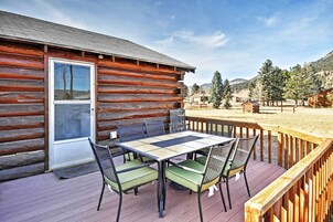 A log cabin with a deck, a table with chairs, and a view of the surrounding landscape.