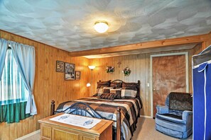 Et hyggeligt værelse med trælofter, en seng med et quiltet dyne, en stol, et skrivebord med en lampe og en dør.