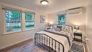 A bedroom with a bed, two bedside tables, a window, and an air conditioning unit.