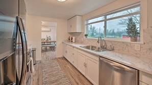 A modern kitchen with a large window, marble countertops, and stainless steel appliances.