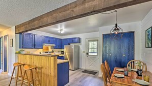 Une cuisine avec des meubles de rangement bleus, un îlot central en bois avec des tabourets, une table à manger avec des chaises et une porte bleue.
