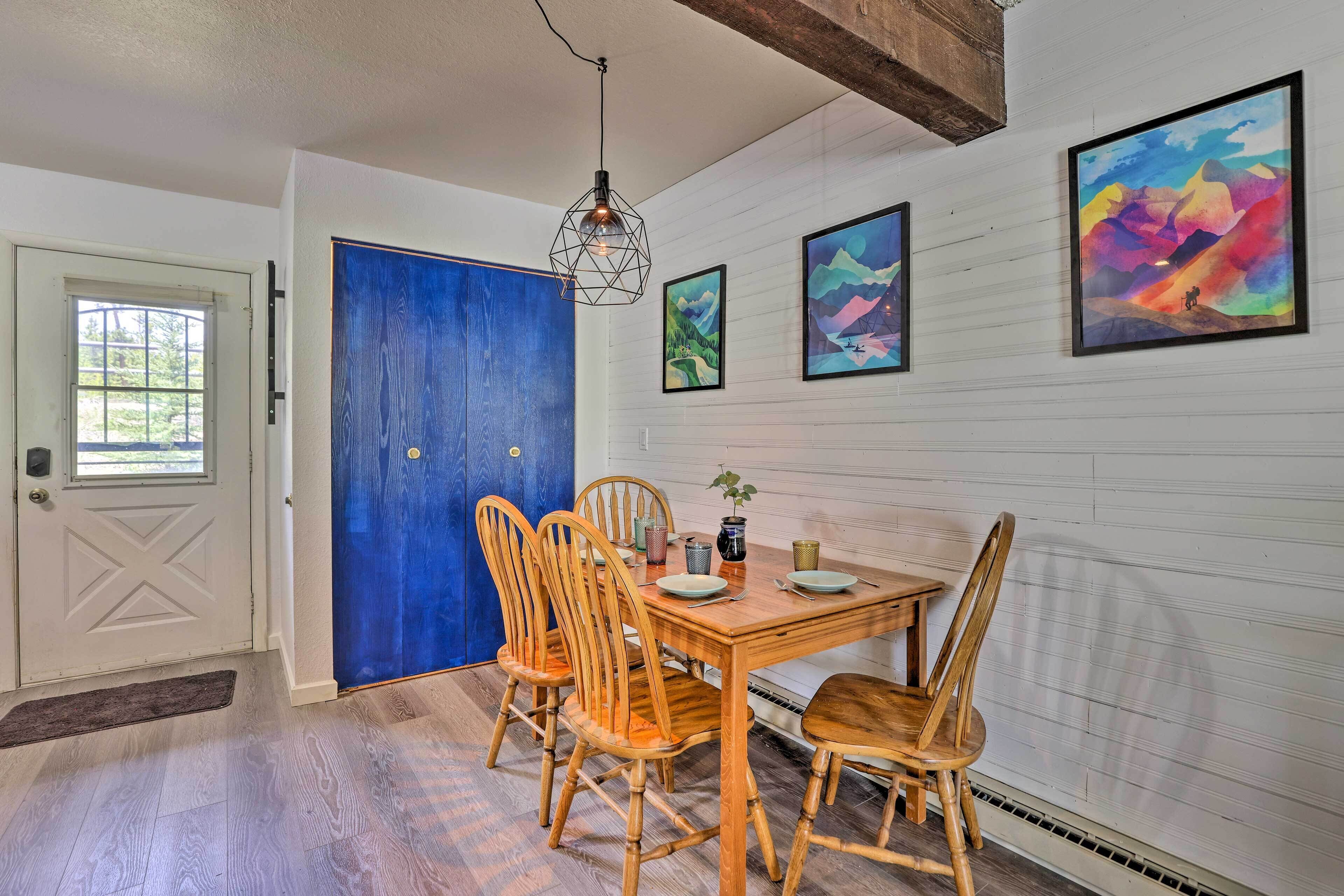 Un comedor con una mesa y sillas de madera, una puerta azul y obras de arte enmarcadas en la pared.