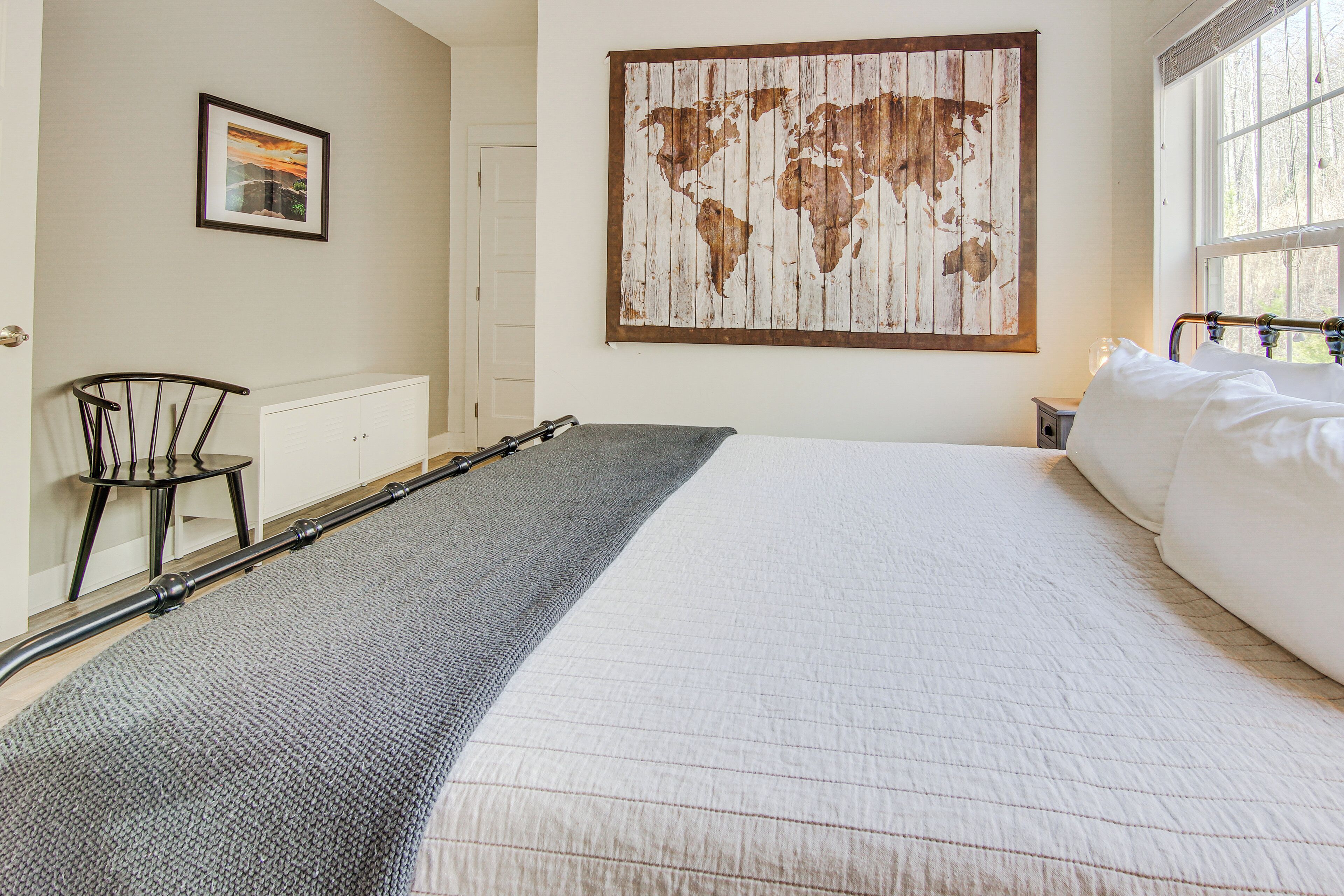 A room with a large bed, a world map on the wall, a small table, and a chair.