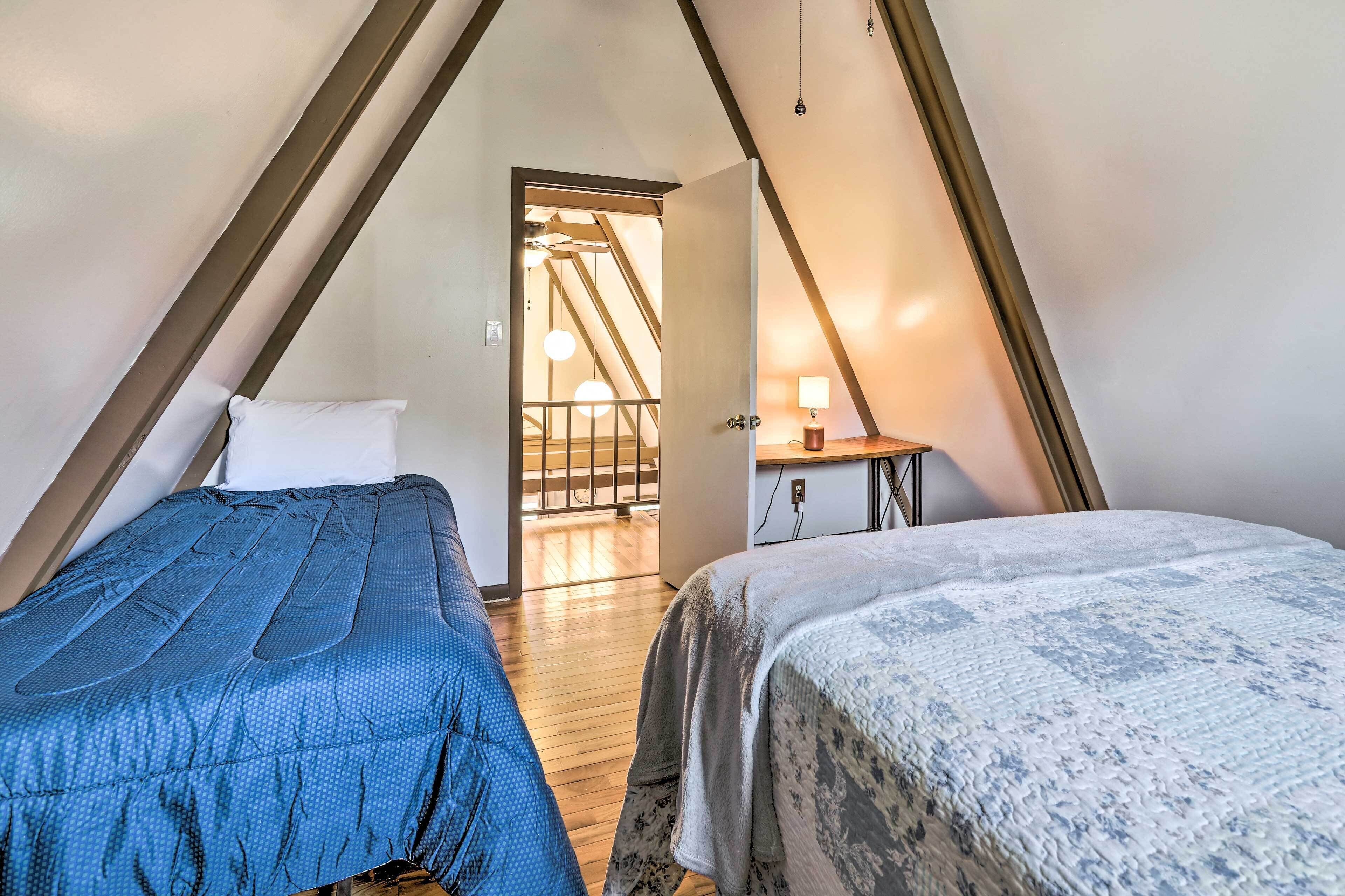 A bedroom with two beds, wooden flooring, a staircase, and a desk with a lamp.