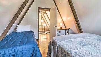 A bedroom with two beds, wooden flooring, a staircase, and a desk with a lamp.