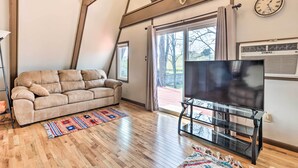 Un salon avec un canapé, un téléviseur posé sur un meuble, un plancher en bois et de grandes fenêtres avec des rideaux.