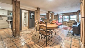 Un vaste espace de vie comprenant une table et des chaises en bois pour la salle à manger, une cheminée et une vue sur l’extérieur grâce à de grandes fenêtres.