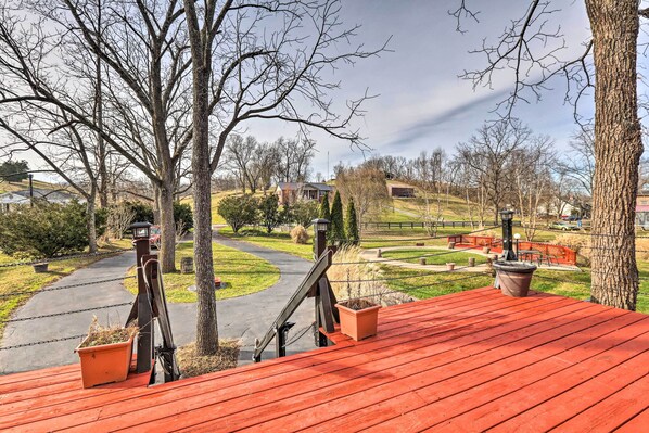 A red wooden deck with potted plants and a metal railing overlooking a park with a winding path and a building in the background.
