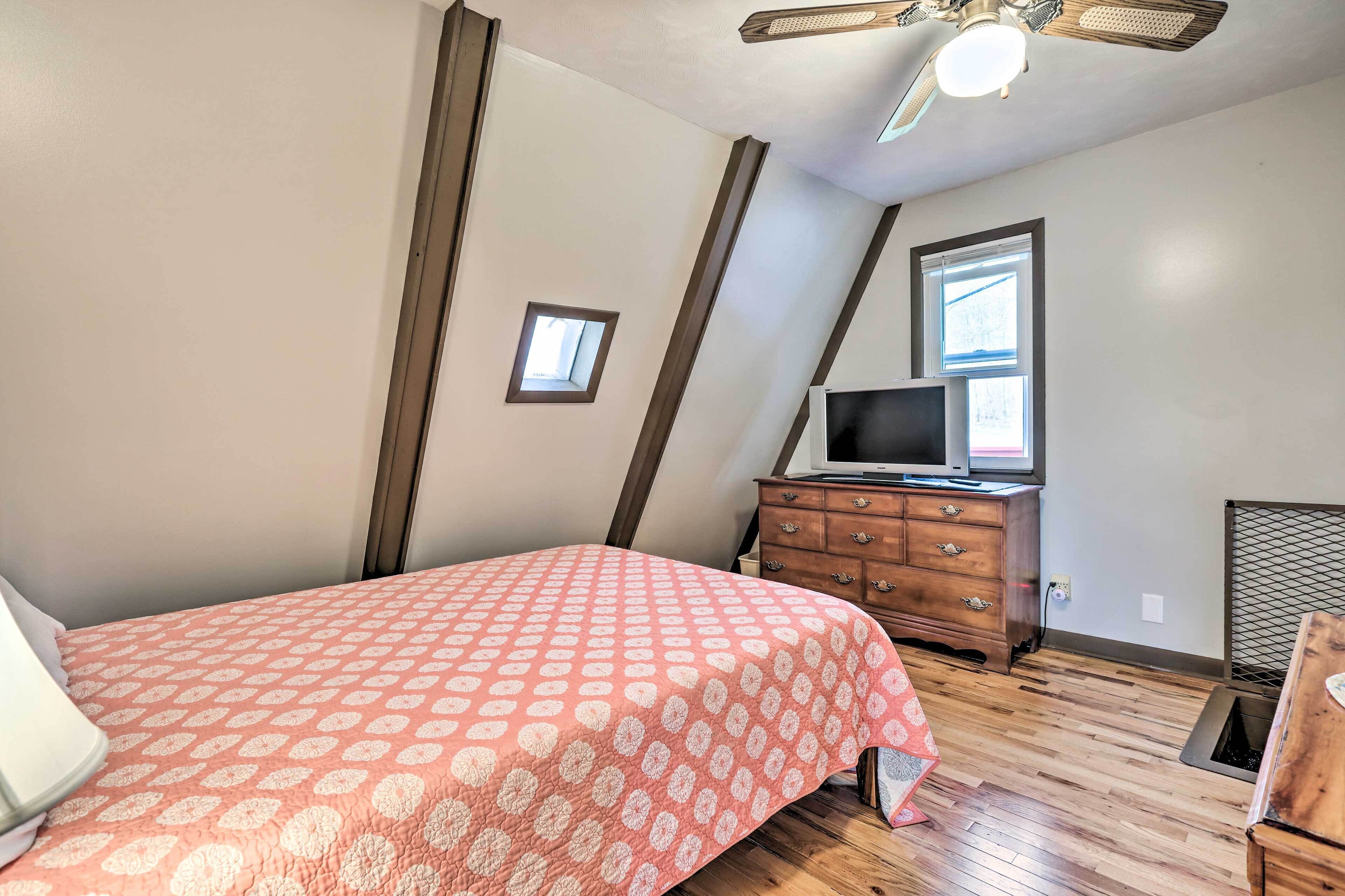 A bedroom with a bed, dresser, TV, and a small window.