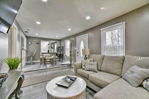 A modern living room with a beige sofa, a round coffee table, and a dining area with a table and chairs.