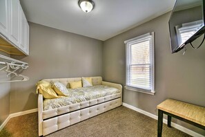 Une chambre à coucher comprenant un lit, un banc, un téléviseur fixé au mur et une fenêtre avec des stores.