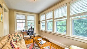A cozy living room with a leather sofa, a wooden coffee table, and a desk with a chair. Large windows with blinds provide ample natural light. - Lovely Apt, 1 Block to Downtown Danville (Danville)