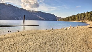 A beach with a wooden pier extending into calm waters, surrounded by forested hills. - Serenity at Scenic Bay: Floating Cottage w/ Views! (Bayview)