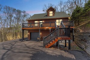 Eine zweistöckige Blockhütte mit Balkon, Treppe und Garage.