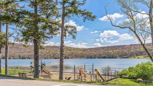 Un parque con juegos infantiles, un lago y una colina boscosa al fondo.
