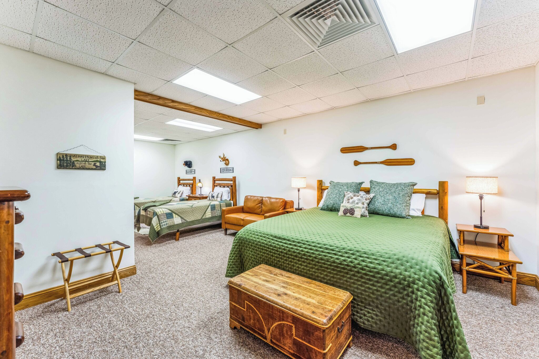 Habitación de hotel con una cama grande, una cama más pequeña, un banco de madera, un aparador y un estante en la pared.