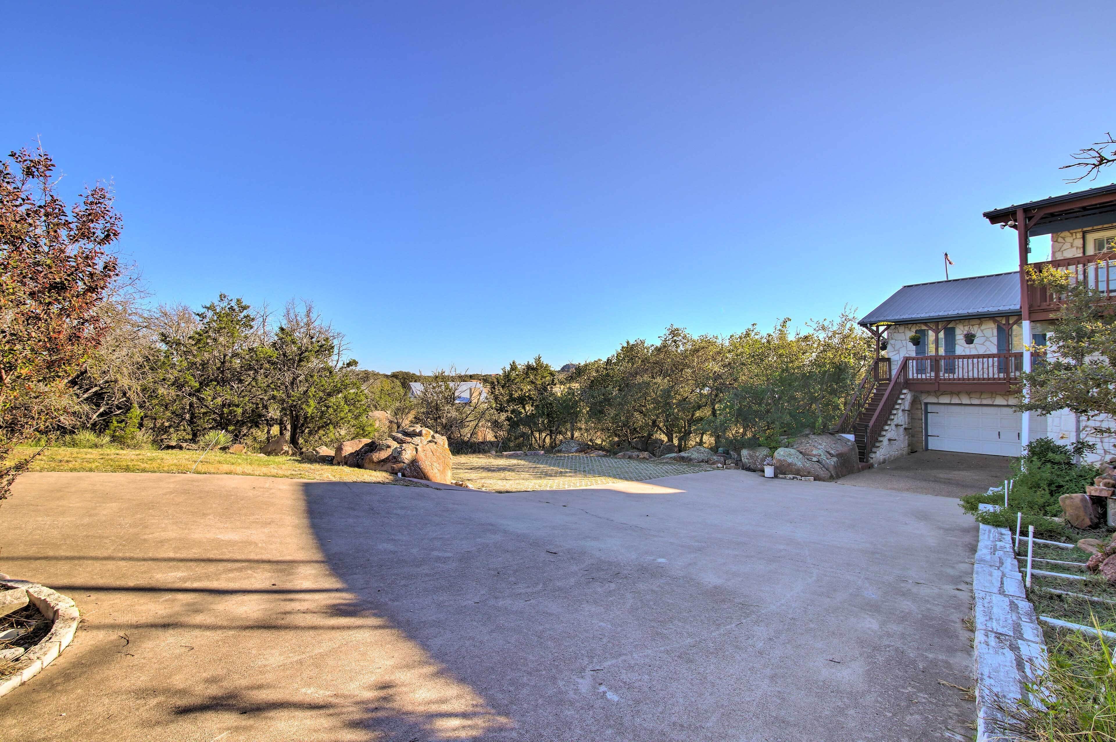 A spacious driveway leading to a two-story house with a garage, surrounded by trees and a clear sky.