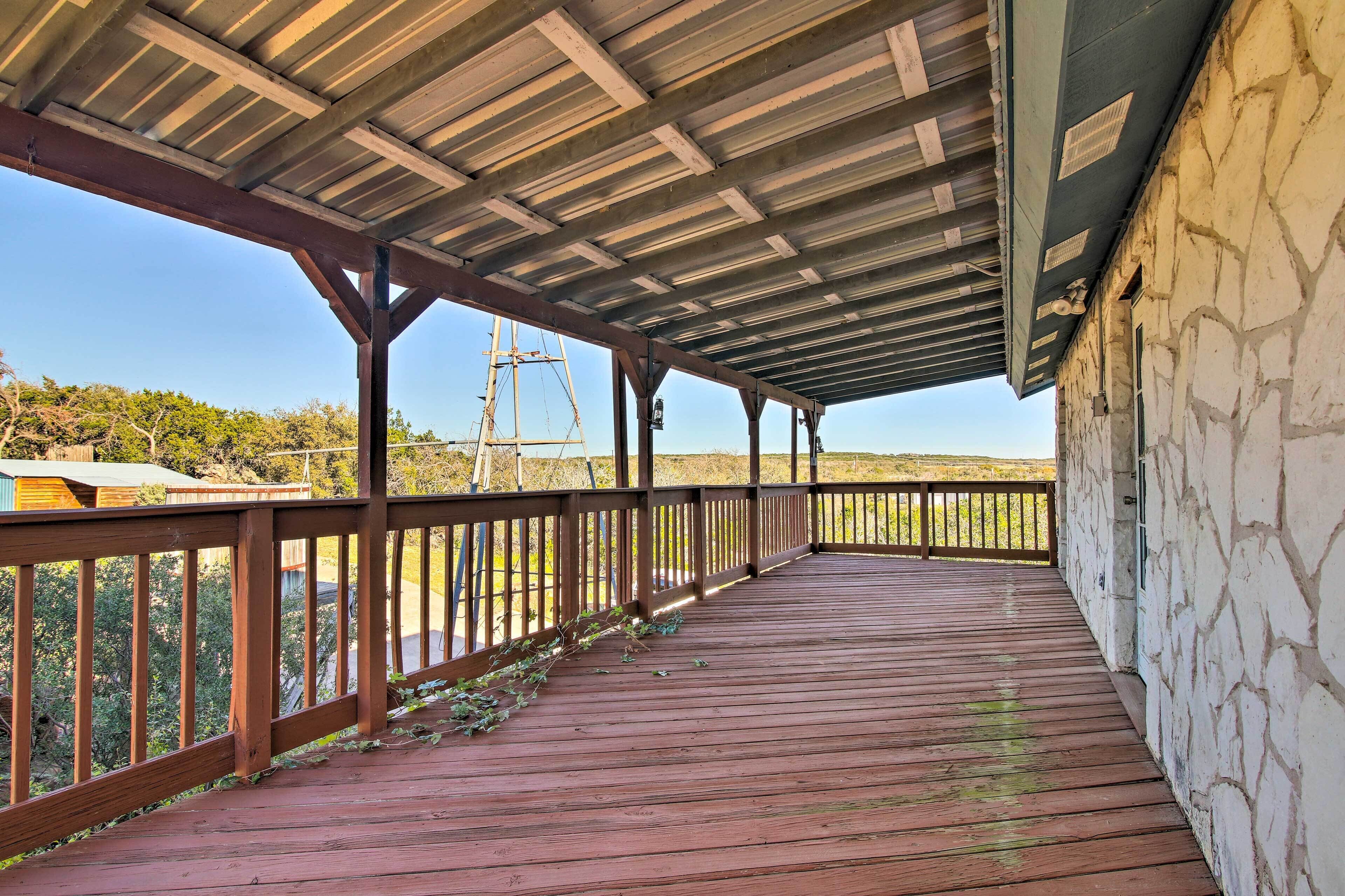 A covered wooden deck with a stone wall on one side, overlooking a hilly landscape.