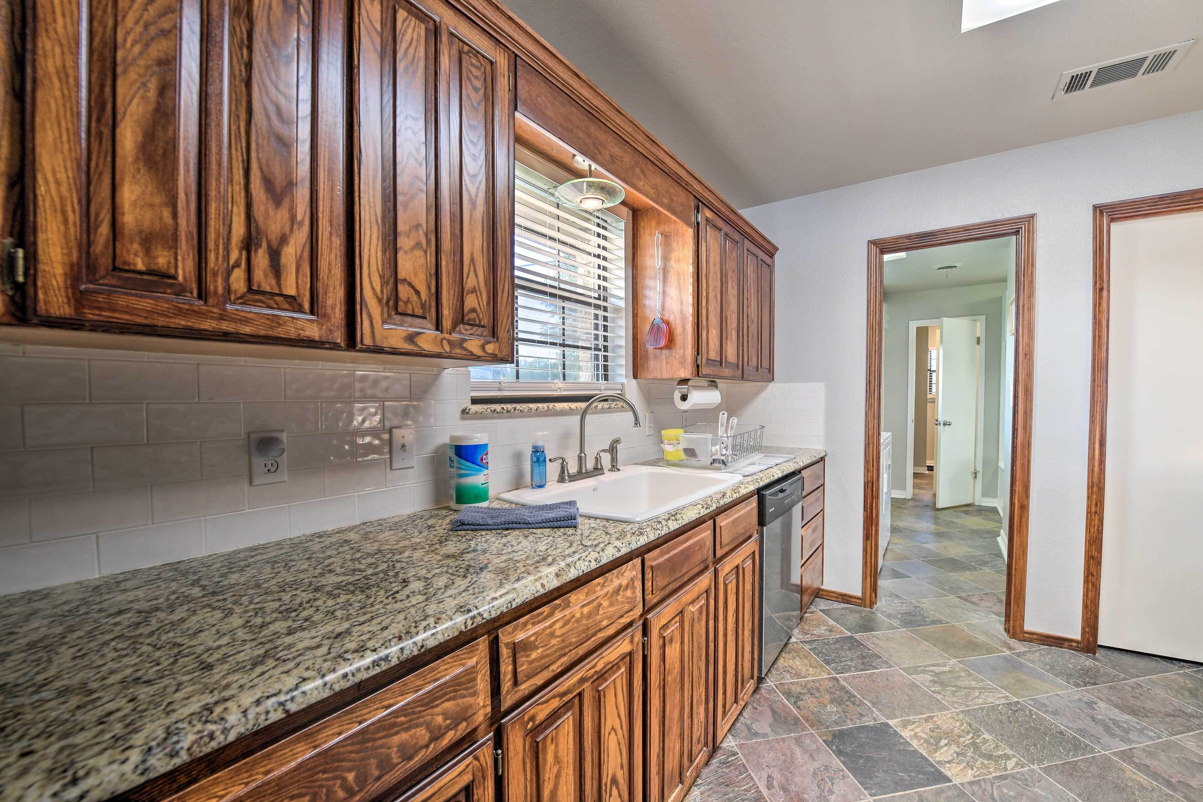A kitchen with wooden cabinets, granite countertops, a sink, and a dishwasher.